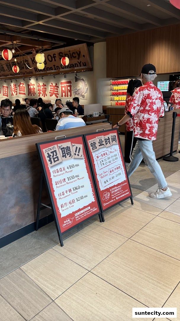 A restaurant interior with patrons and A-frame signs advertising job openings and business hours.