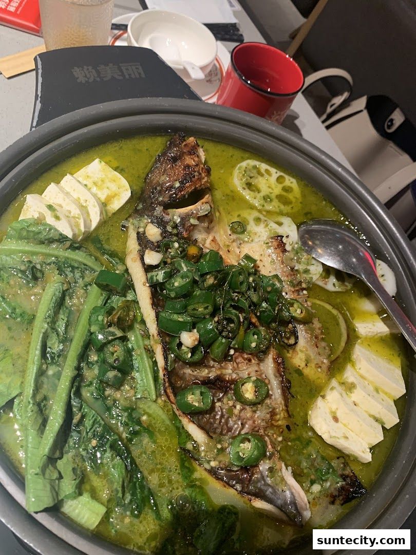 A close-up of a flavorful grilled fish dish with vegetables and tofu in a green broth.