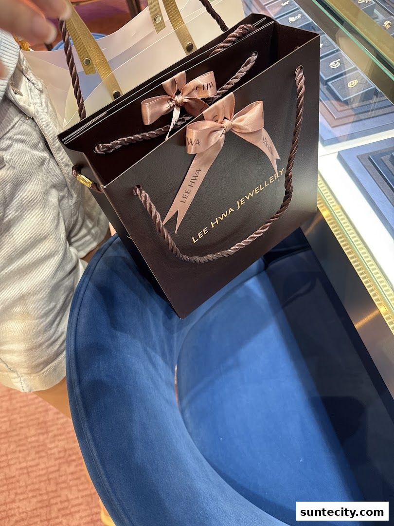 A person holding shopping bags from Lee Hwa Jewellery in a store.