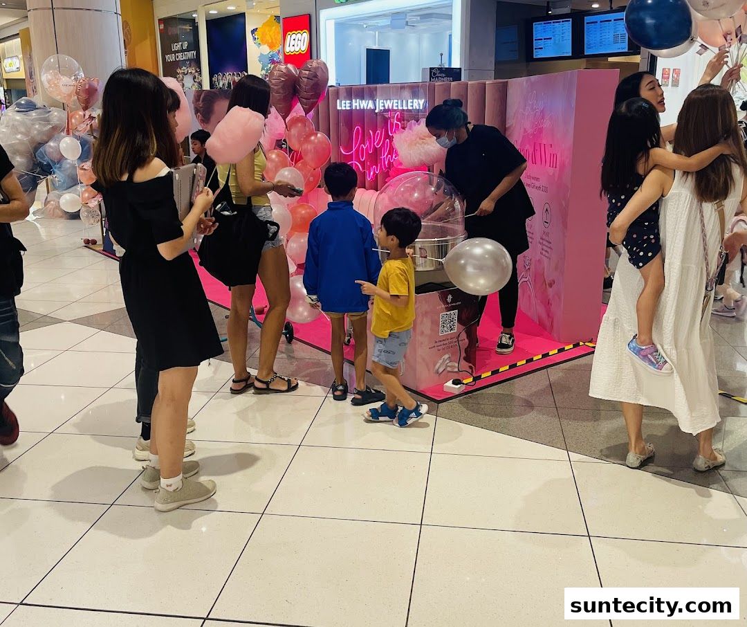 People gathered around a pink booth with balloons, possibly at a promotional event.