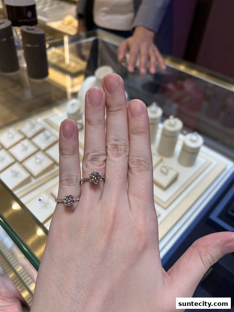 A hand wearing two diamond rings is shown in front of a jewelry display case.