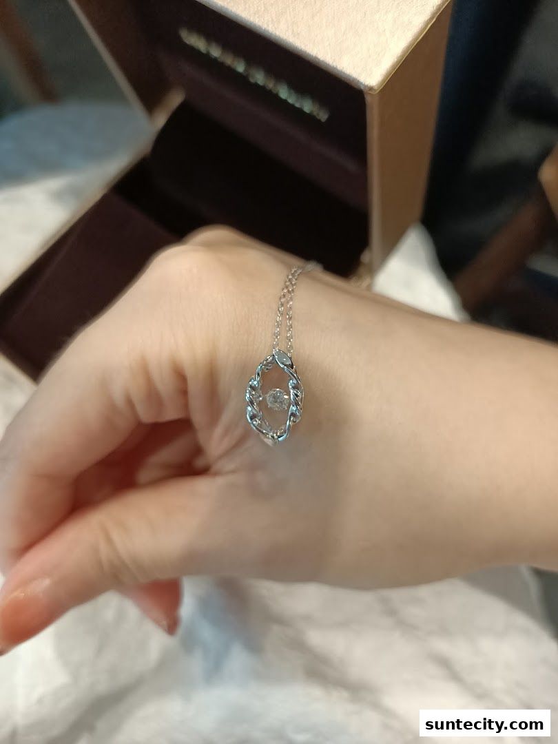 A hand wearing a delicate silver necklace with a sparkling pendant.