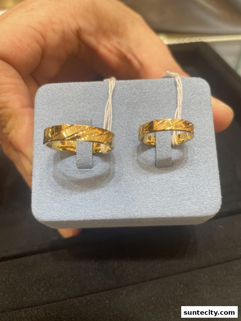 A hand holds two gold rings with intricate patterns on a display stand.