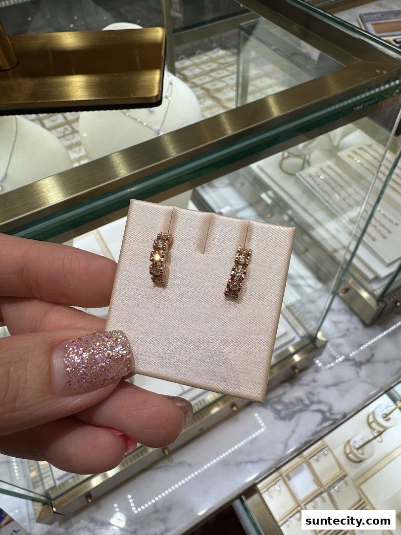 A hand holding a pair of diamond hoop earrings in front of a jewelry display case.