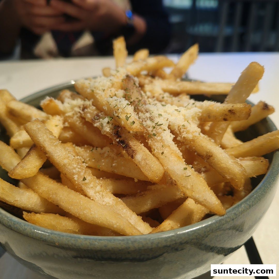 A close-up shot of a bowl of golden-brown french fries topped with grated cheese and herbs.