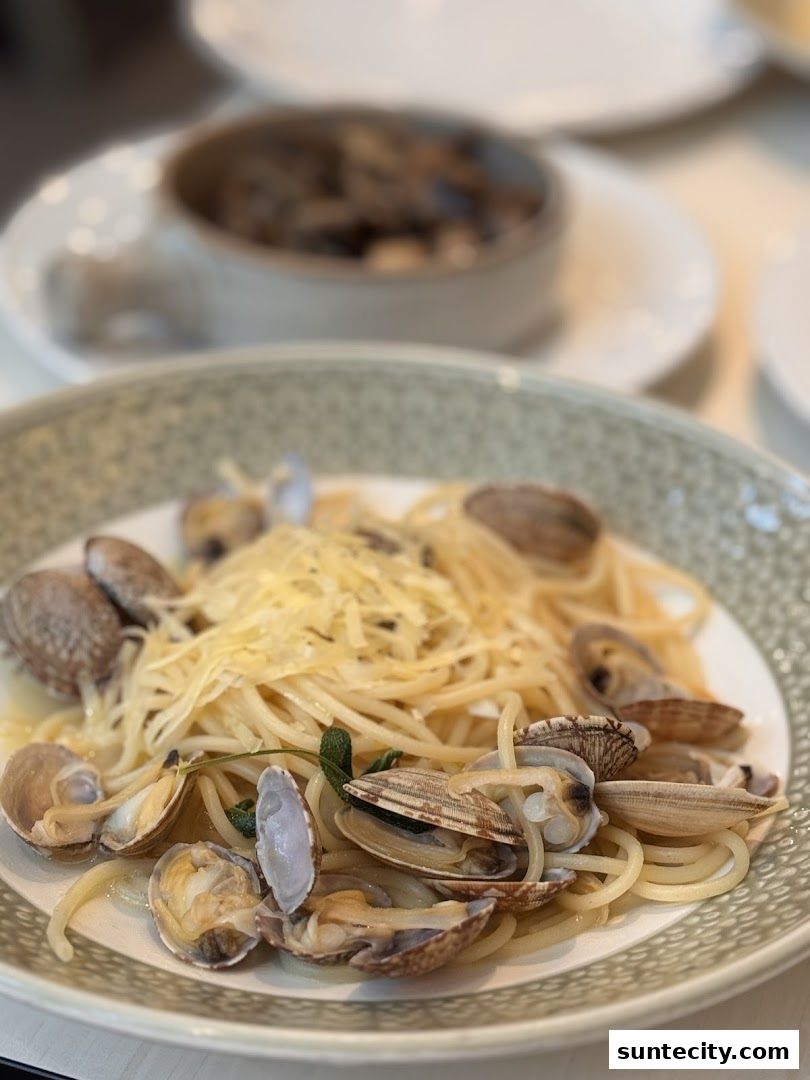 A close-up of spaghetti with clams and grated cheese, garnished with herbs.