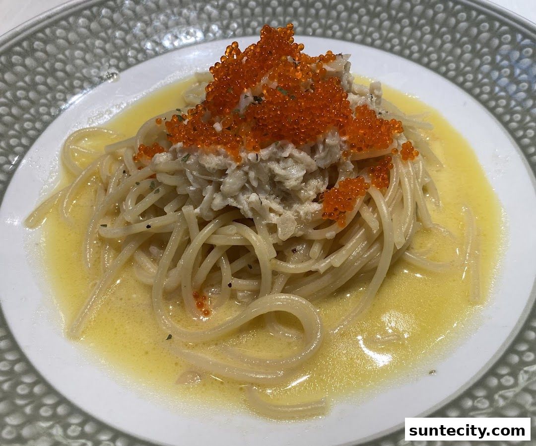 A close-up of spaghetti topped with crab meat and bright orange tobiko.