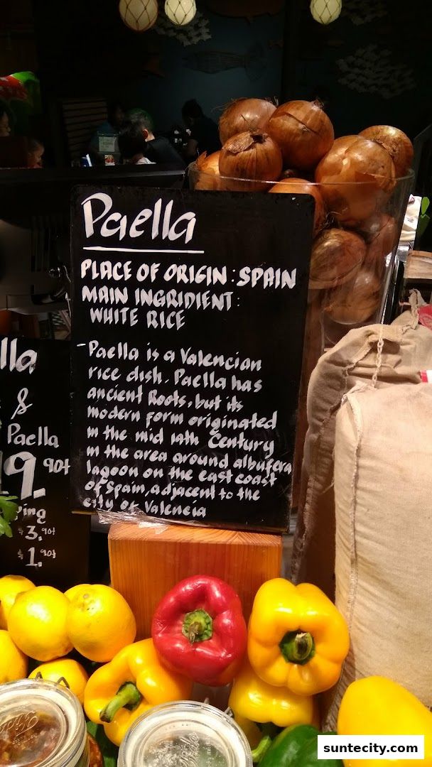 A sign describing Paella, with ingredients like rice, peppers, and onions visible.