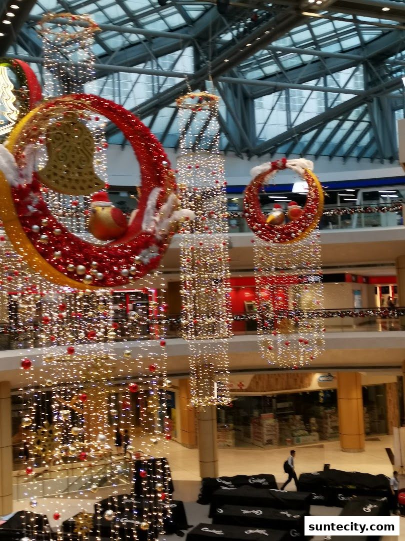 Festive Christmas decorations with lights and ornaments hang in a mall atrium.