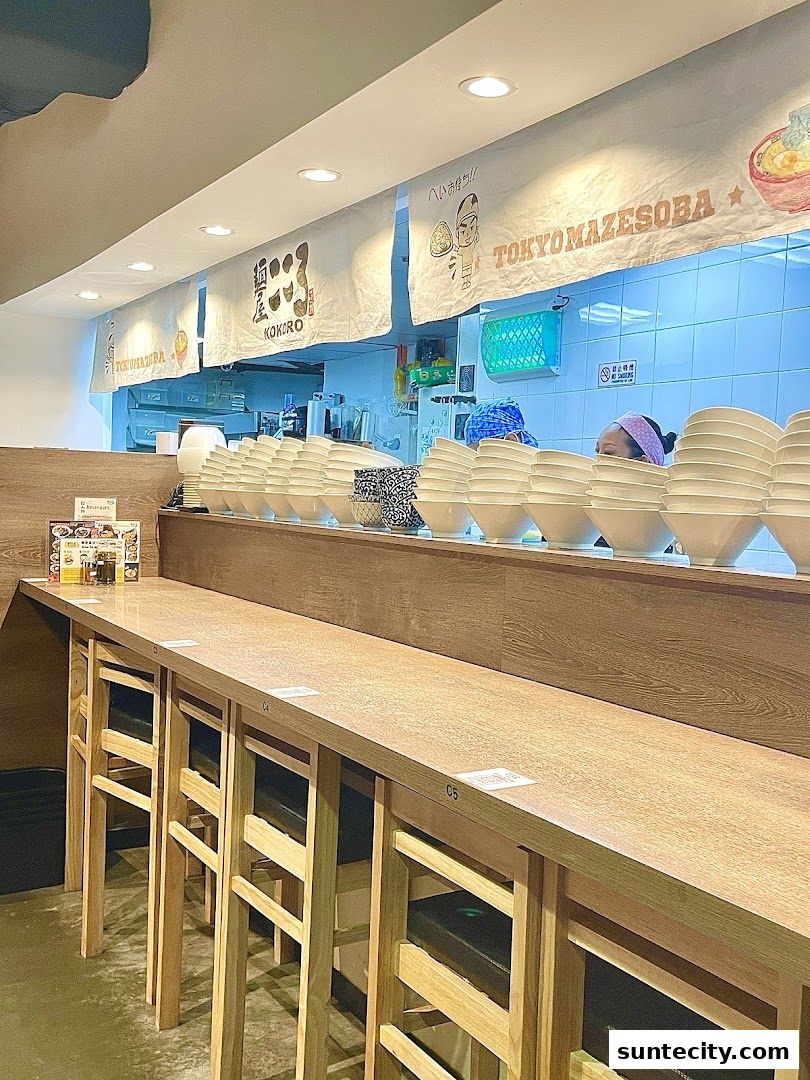 Interior view of Menya Kokoro with a long counter, chairs, and stacked bowls.