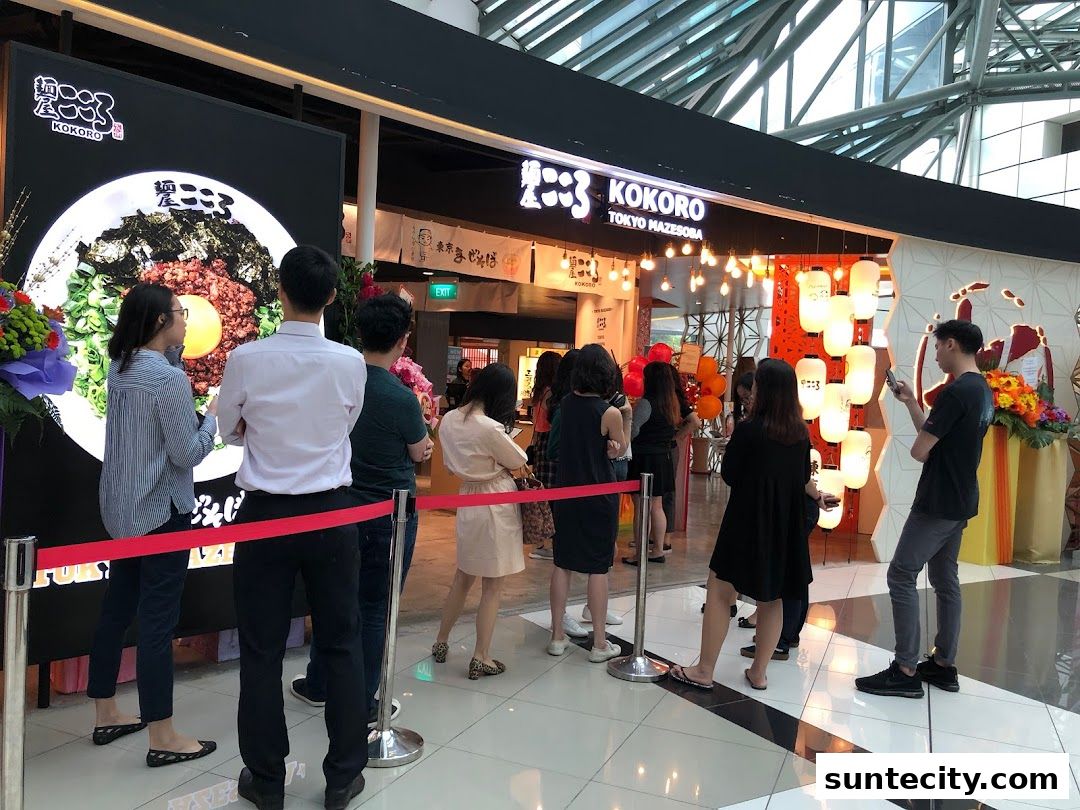 People queuing outside a Japanese restaurant with a large display of food.