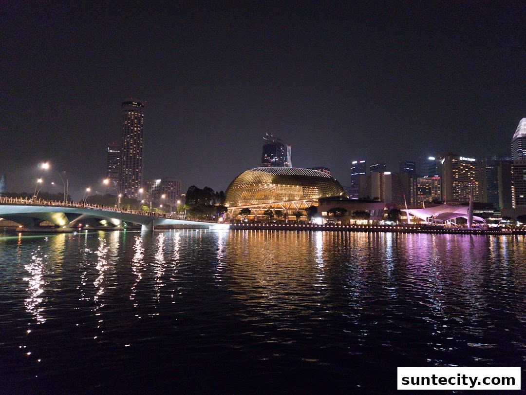 A nighttime cityscape view of a waterfront with illuminated buildings and a bridge.
