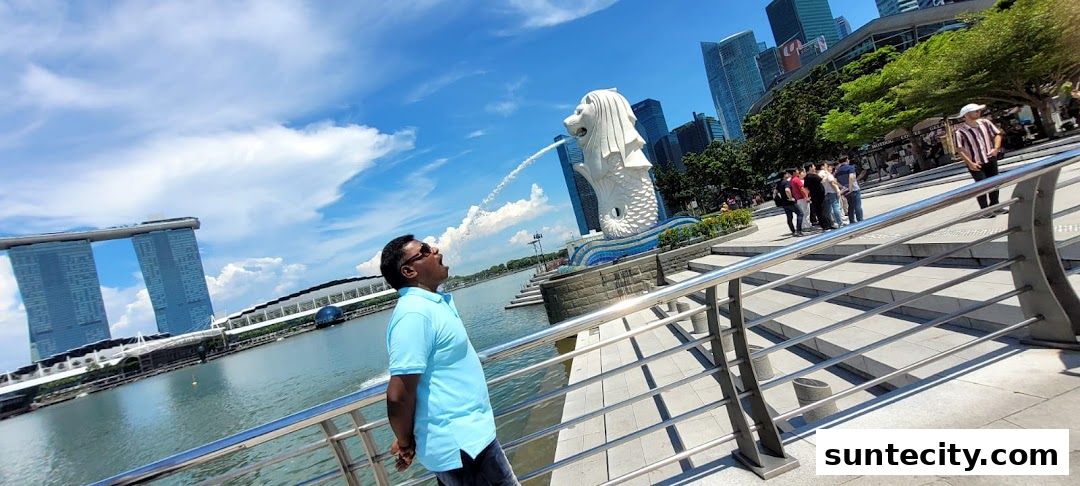 A man drinks water from the Merlion statue with Marina Bay Sands in the background.