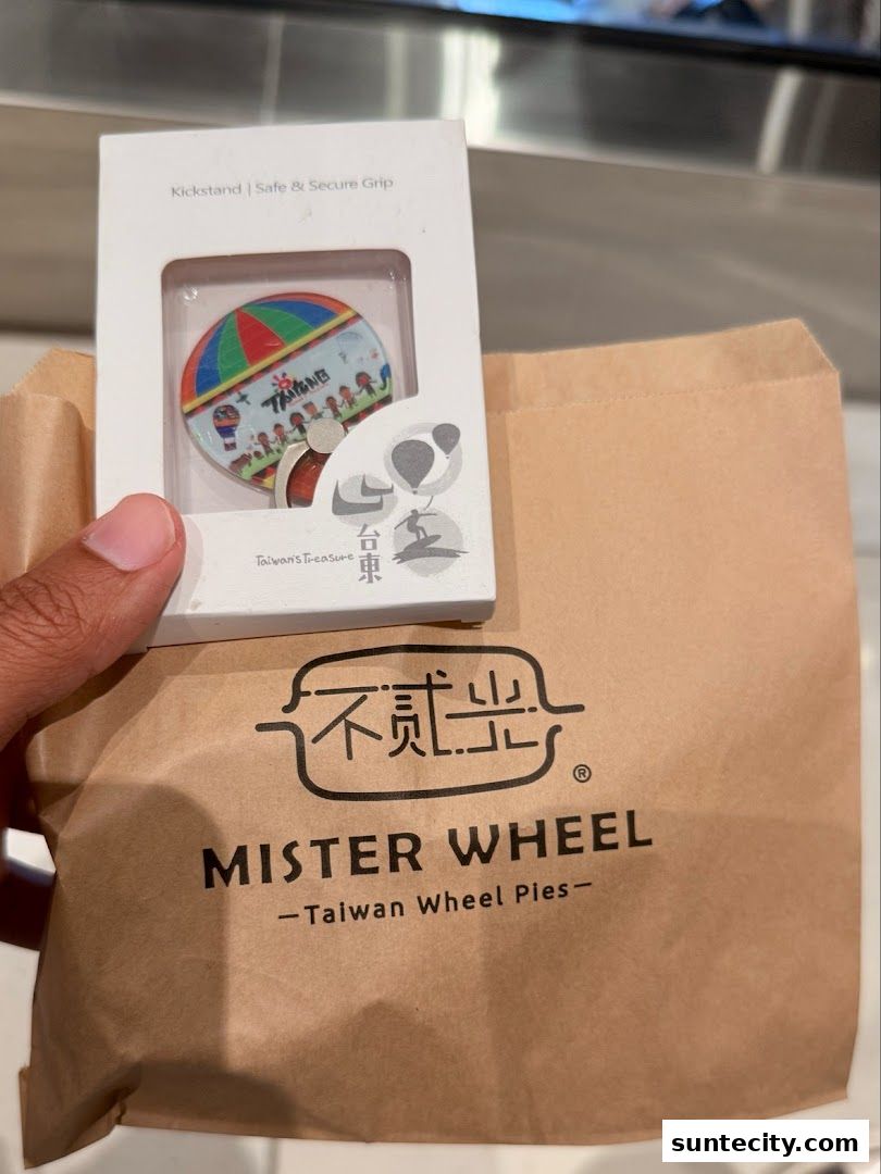 A hand holds a branded paper bag with a phone accessory box on top.