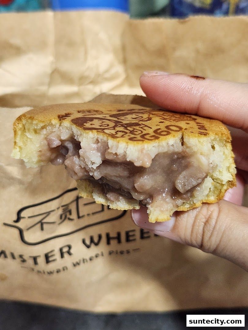 A hand holds a bite of a Taiwanese wheel cake filled with taro paste.