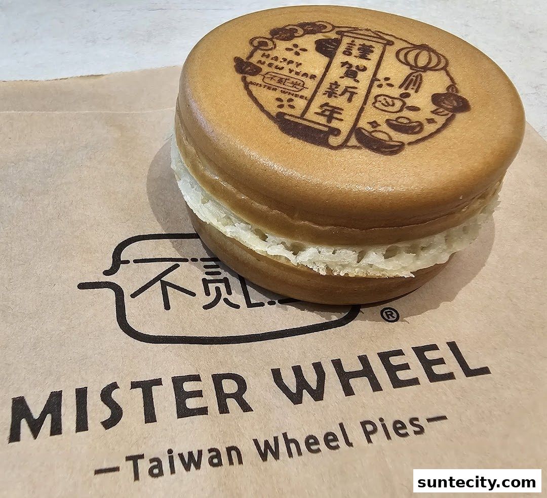 A close-up of a Taiwan Wheel Pie with 'Happy New Year' branding on a Mister Wheel paper bag.