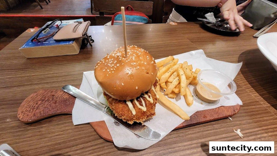 A delicious-looking burger with fries and dipping sauce on a wooden board.