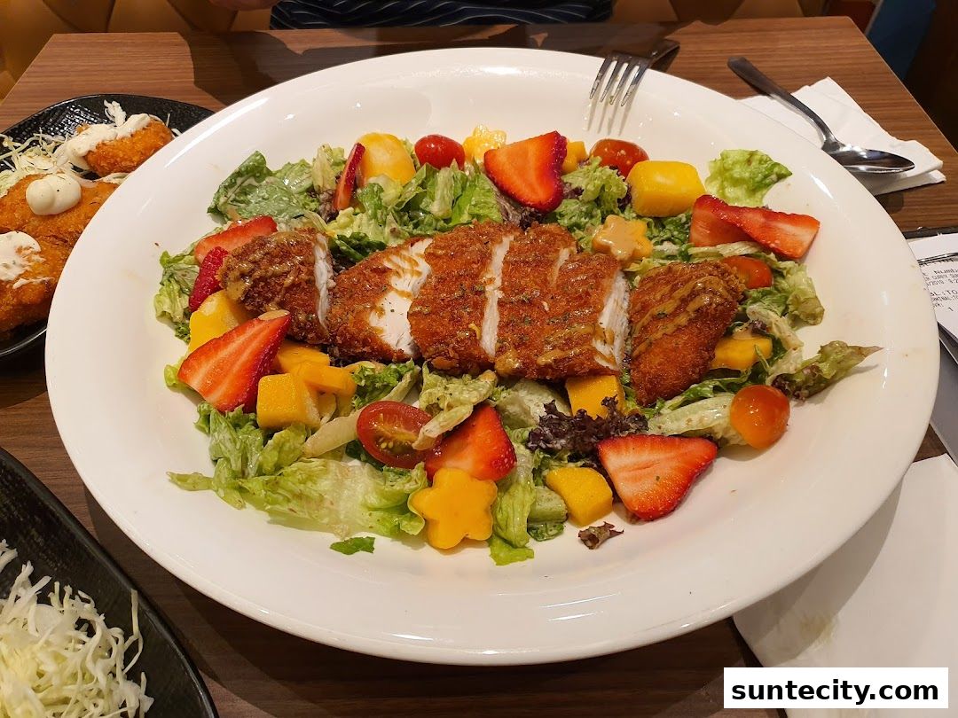 A delicious salad with fried chicken, strawberries, mango, and cherry tomatoes.