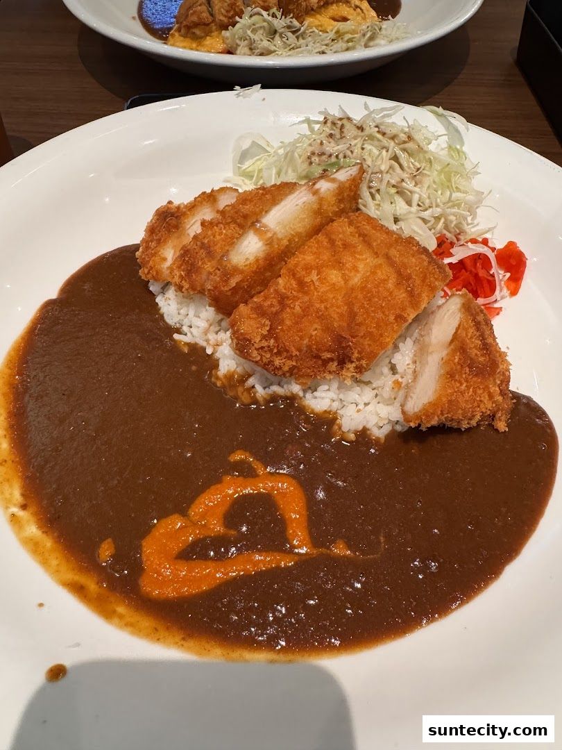 A plate of Japanese curry with rice, crispy chicken katsu, and a side salad.