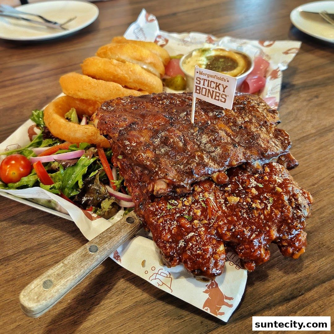 A plate of sticky pork ribs with onion rings, salad, and dipping sauce.