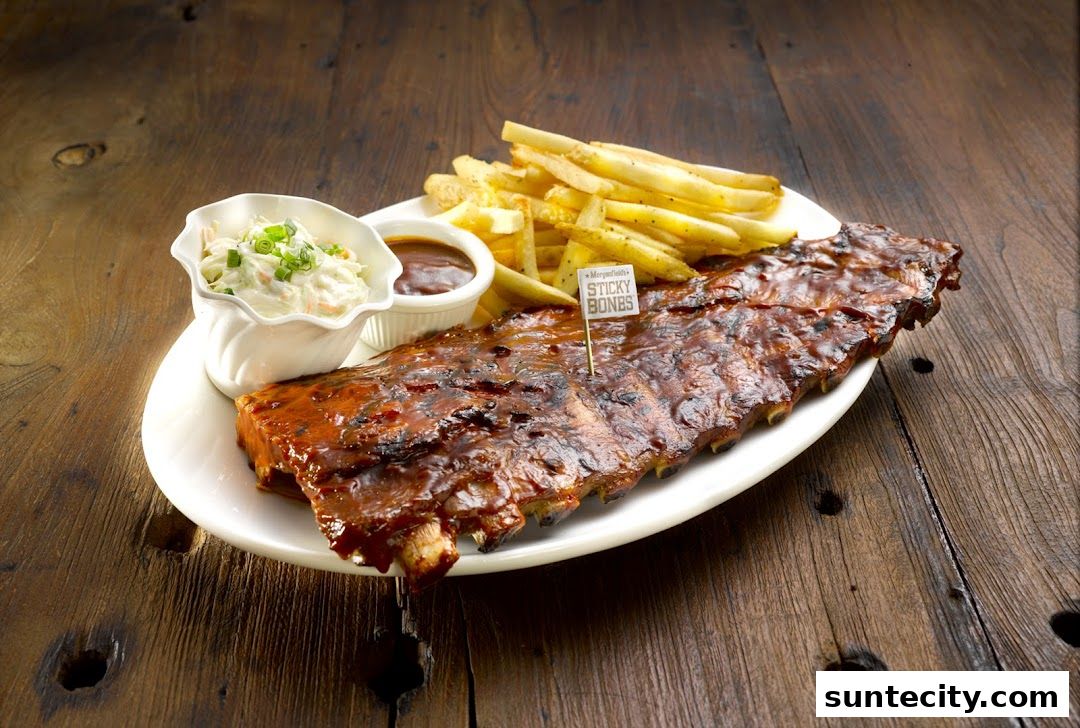 A plate of sticky pork ribs with fries, coleslaw, and dipping sauce.