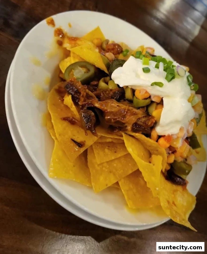 A plate of loaded nachos with pulled meat, jalapenos, corn, and sour cream.