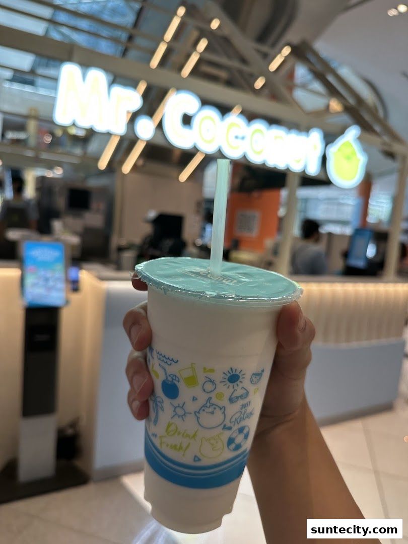 A hand holds a coconut drink in front of the Mr. Coconut shop.