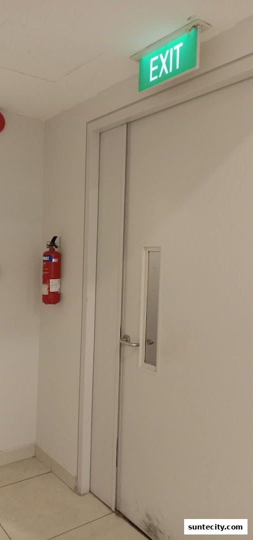 A white door with a fire extinguisher mounted on the wall and an illuminated exit sign above.