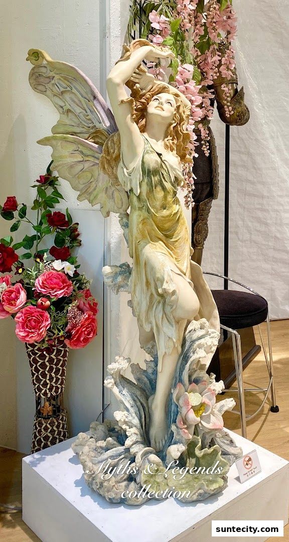 A statue of a fairy with wings, surrounded by flowers and a knight's armor.