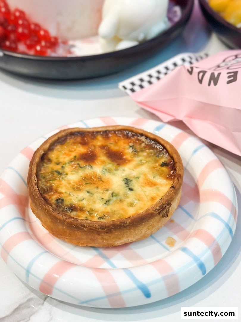 A delicious quiche is served on a pastel-striped plate, with other cafe treats in the background.