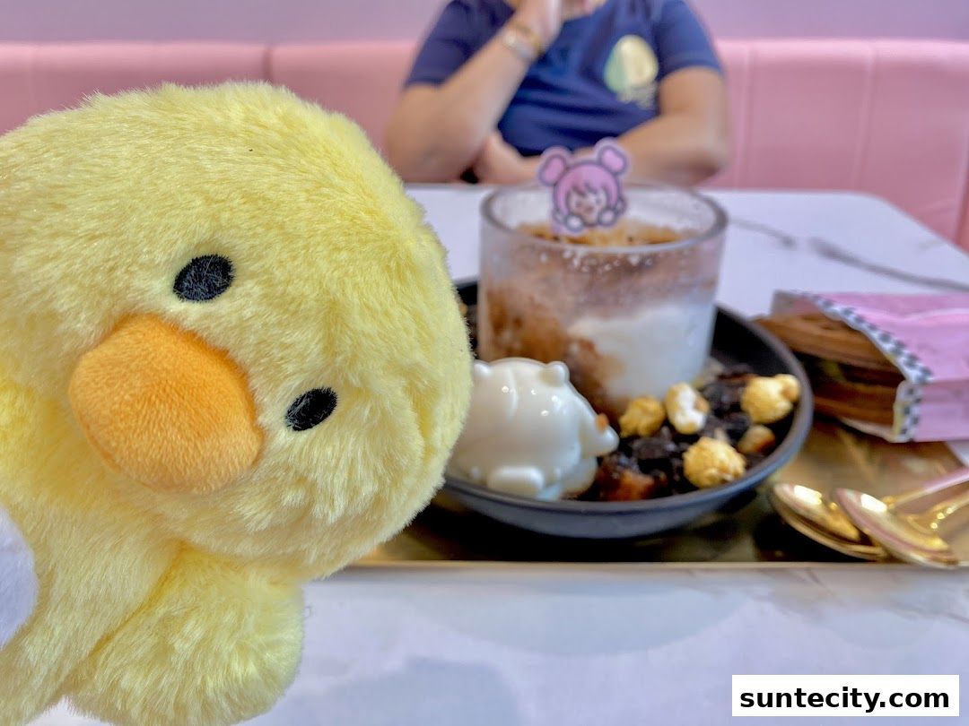 A fluffy yellow duck plush toy sits next to a dessert with popcorn and a cute character topper.
