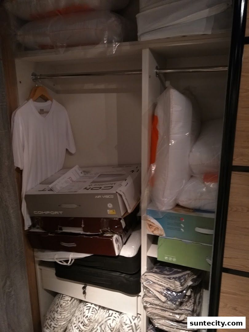 A closet filled with bedding, pillows, and a white t-shirt on a hanger.