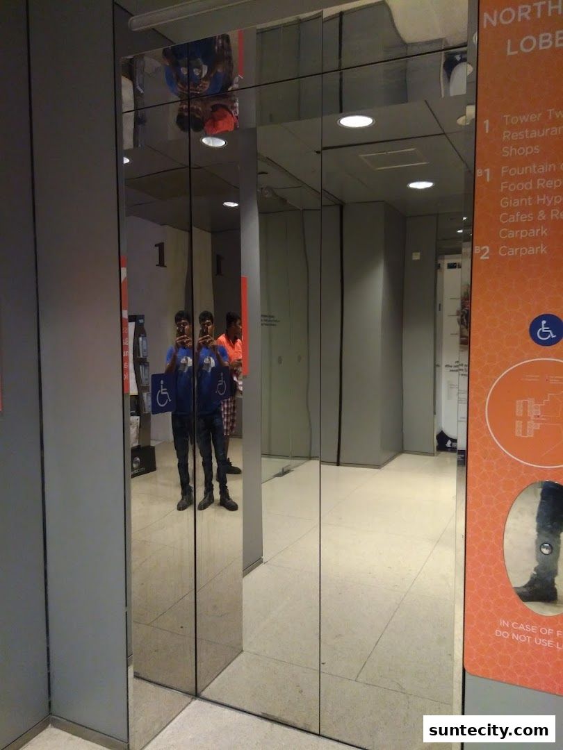 Reflections in mirrored elevator doors show people and a mall directory.