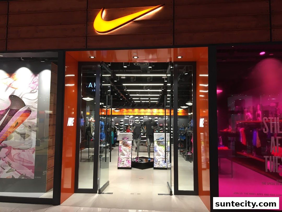 The entrance of a Nike store with a prominent illuminated logo and displays of athletic wear.