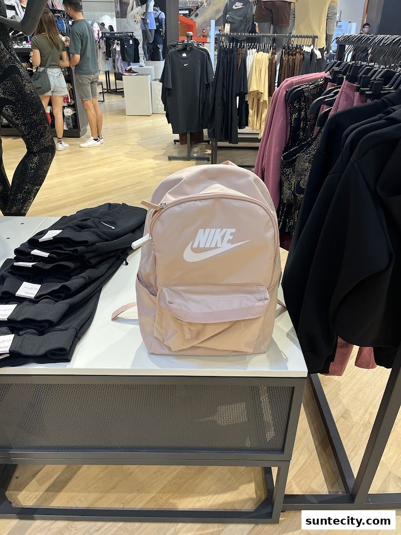 A pink Nike backpack is displayed on a table with black apparel in a retail store.