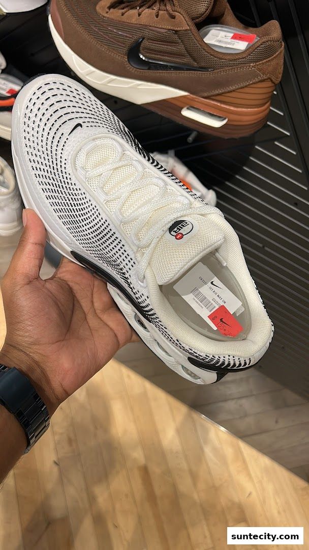A hand holds a white Nike Air Max sneaker with black detailing and a price tag.