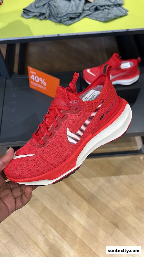 A hand holds a bright red Nike running shoe with white accents and a white sole.