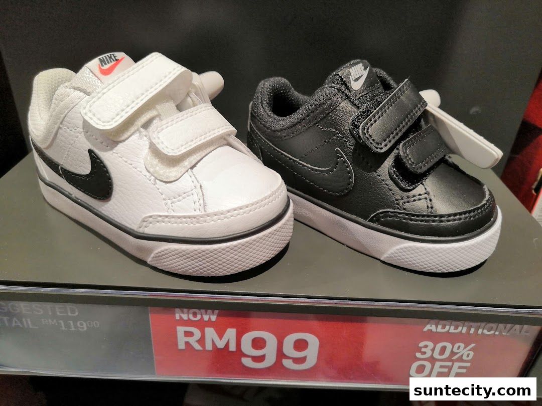 Two pairs of Nike baby sneakers, one white and one black, displayed on a shelf with a sale tag.