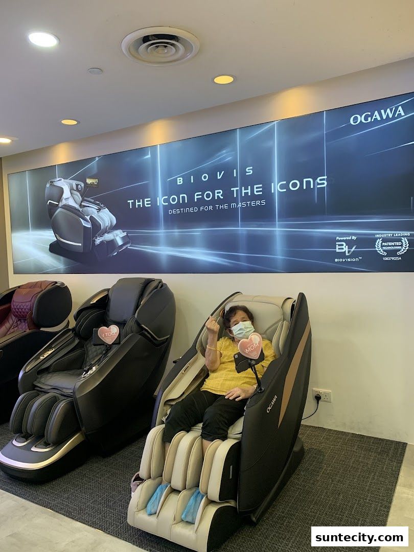 A woman sits in an Ogawa massage chair, with other chairs and a large advertisement in the background.