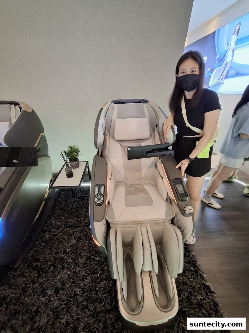 A woman stands next to a luxurious massage chair in a modern retail setting.