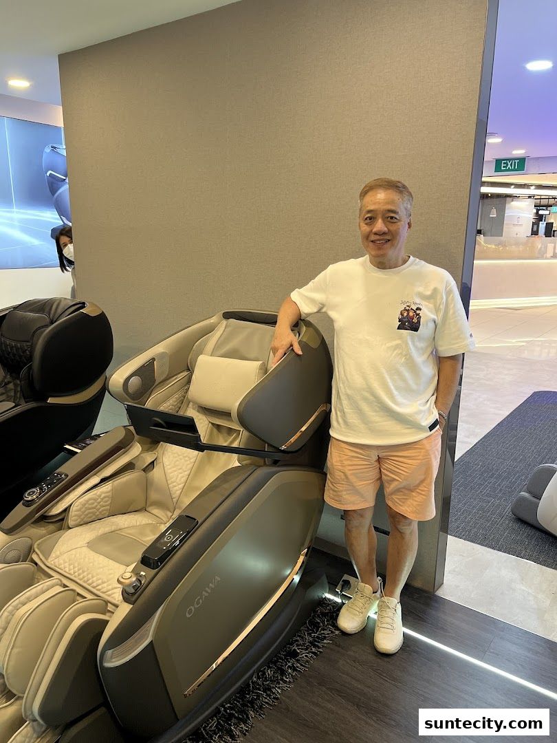 A man poses next to a luxurious Ogawa massage chair in a modern retail store.