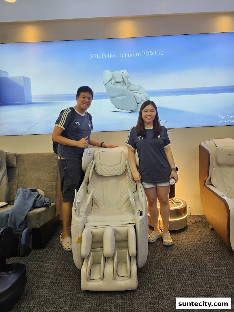 Two people stand next to a white massage chair in a store, with a large screen displaying a massage chair.