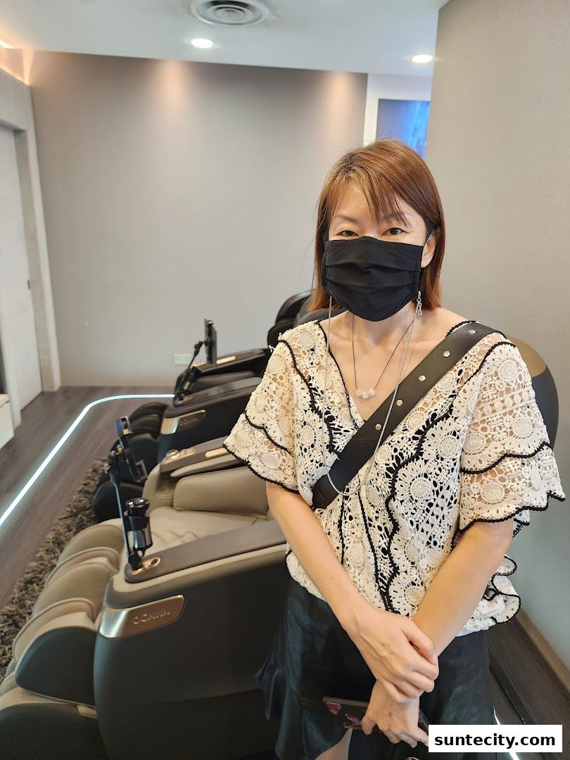 A woman wearing a mask stands in front of several massage chairs at Ogawa.