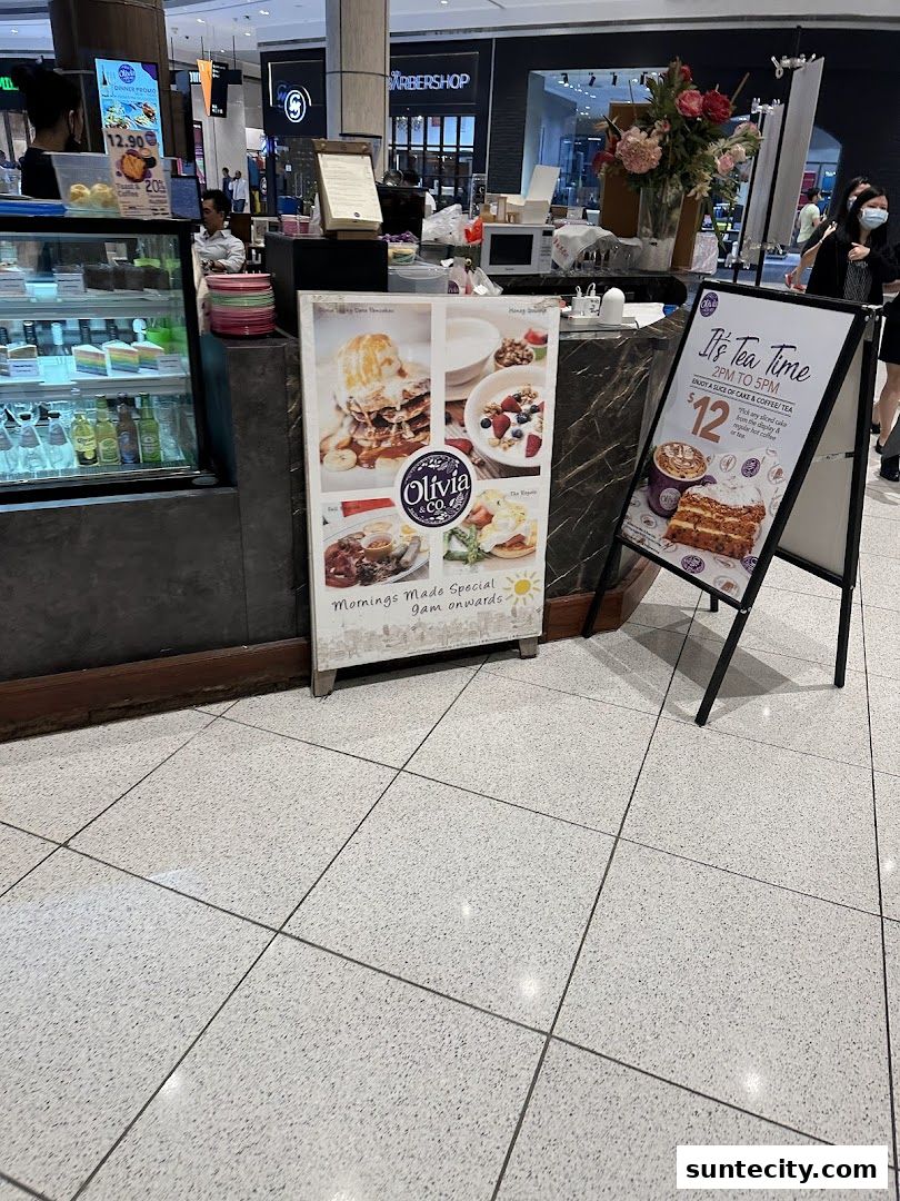 A cafe counter with a display of cakes and promotional signs for Olivia & Co.
