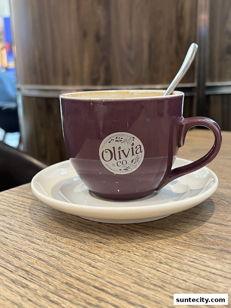 A close-up of a purple coffee cup with the Olivia Co. logo and a spoon on a saucer.