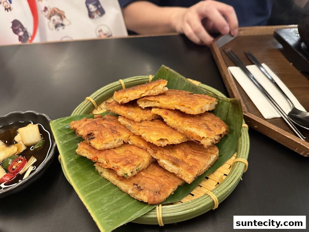 A plate of savory pancakes served with a side of dipping sauce and pickled vegetables.