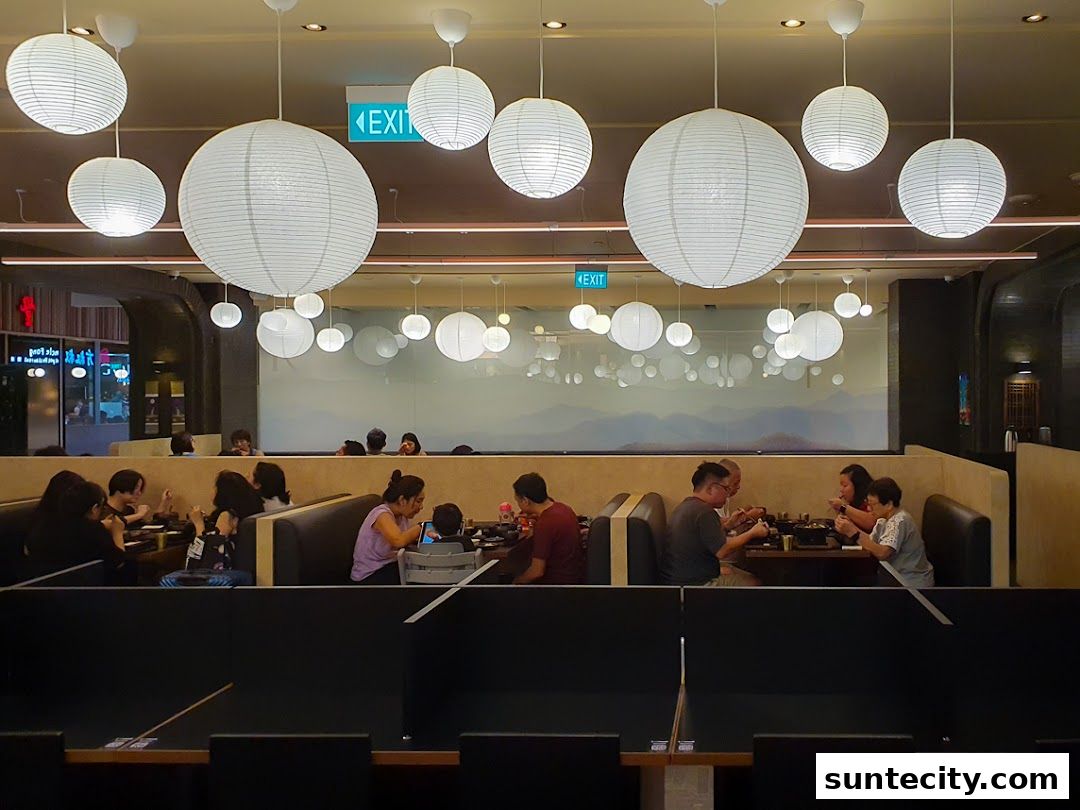 Diners enjoy a meal in a restaurant with many round paper lanterns hanging from the ceiling.