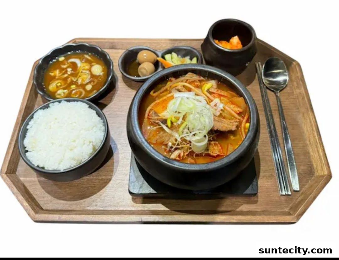 A Korean meal set featuring a hearty stew, rice, and side dishes on a wooden tray.
