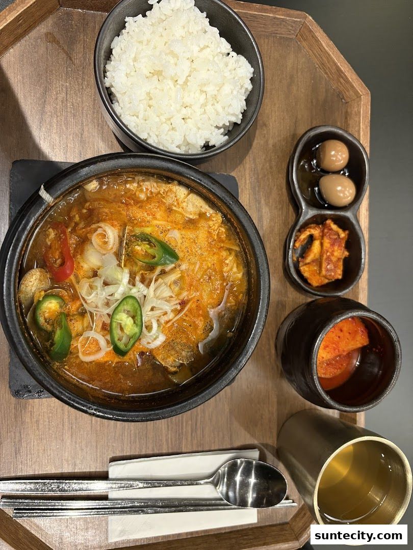 A steaming bowl of Korean stew with rice, kimchi, and pickled eggs served on a wooden tray.