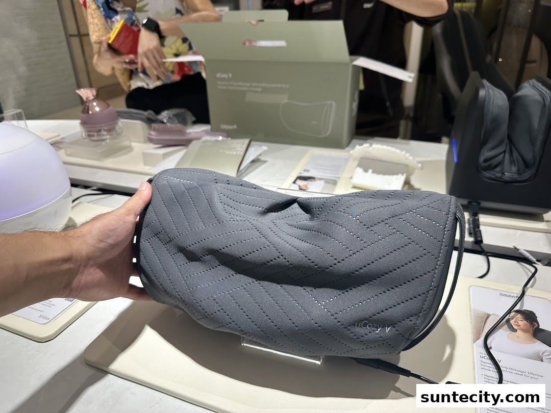 A hand holds a grey uCozy V massage pillow with a foot massager in the background.